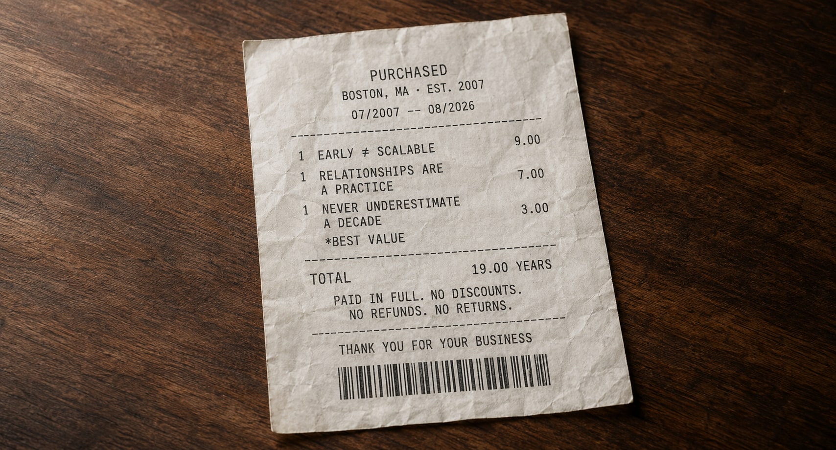 A worn paper receipt on a dark wooden table. The header reads PURCHASED, Boston MA, Est. 2007, dated 07/2007 to 08/2026. Three line items are listed: early does not equal scalable, 9.00; relationships are a practice, 7.00; never underestimate a decade, 3.00, marked best value. The total reads 19.00 years, paid in full, no discounts, no refunds, no returns. At the bottom: thank you for your business, above a barcode.